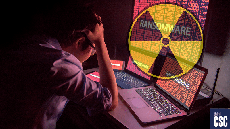 nuclear ransomware - stressed worker with hands on his head looking at laptops and mobile devices that have been encrpted with ransomware overlayed with a nuclear warning symbol